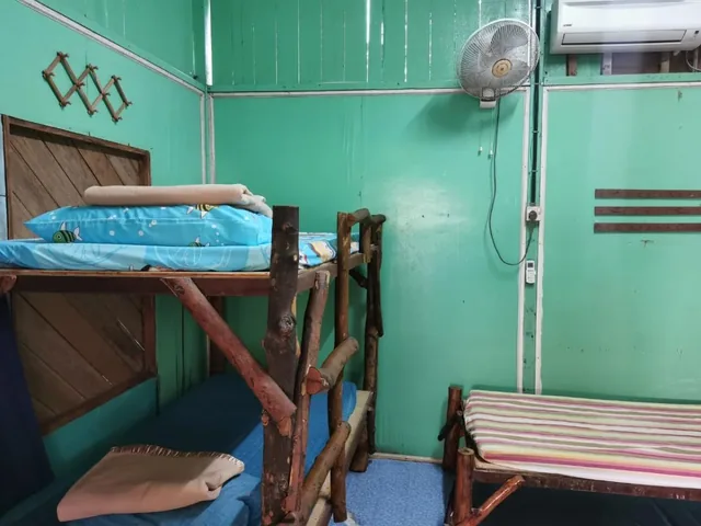 Aguna Resort dorm interior with a wooden bunk bed, bench, fan and air-conditioning unit