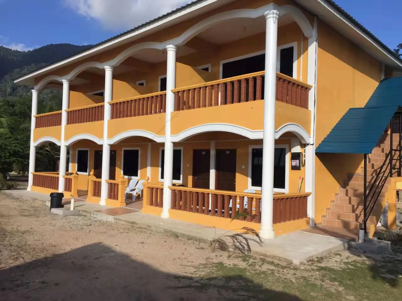 Yellow two-storey Idaman Beach Holiday Resort building with open verandas and a forested hill behind