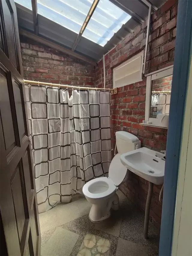 Impian Inn quad room bathroom with exposed brick walls, a basin and a curtained shower