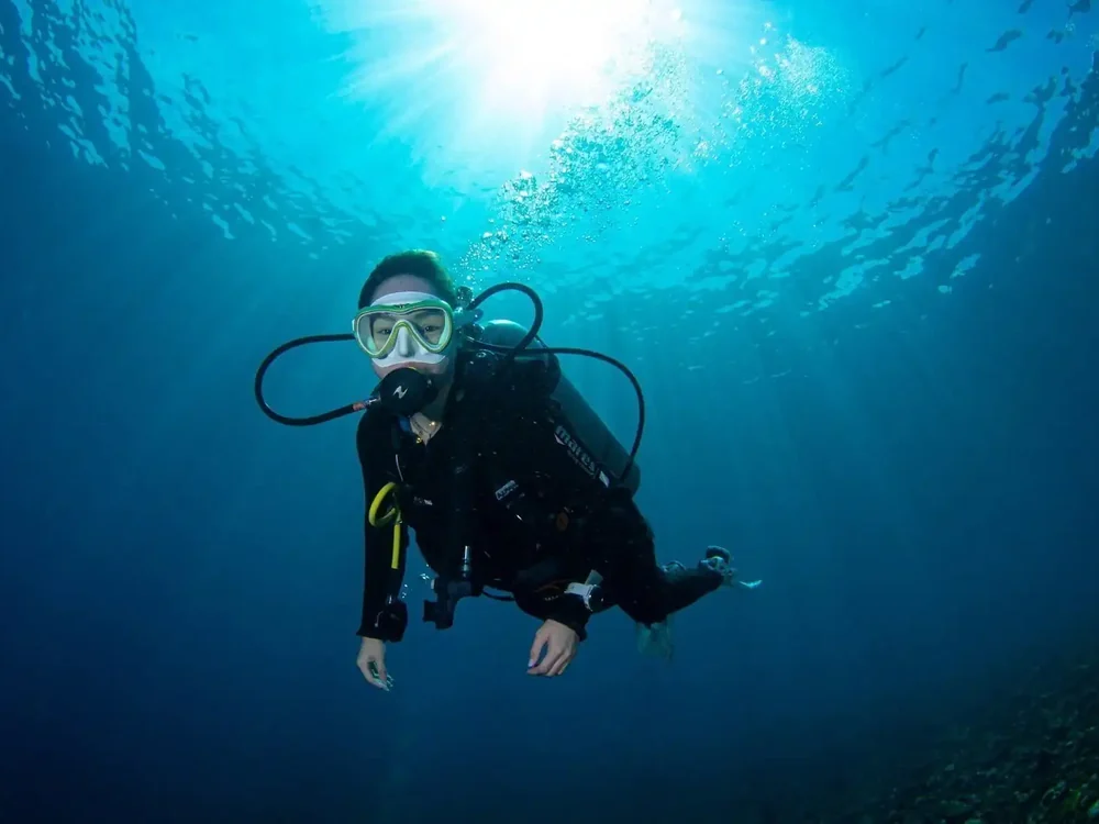 A diver swimming through sunlit blue water
